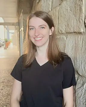 Here's an alt tag for the image: Smiling woman in black scrubs.